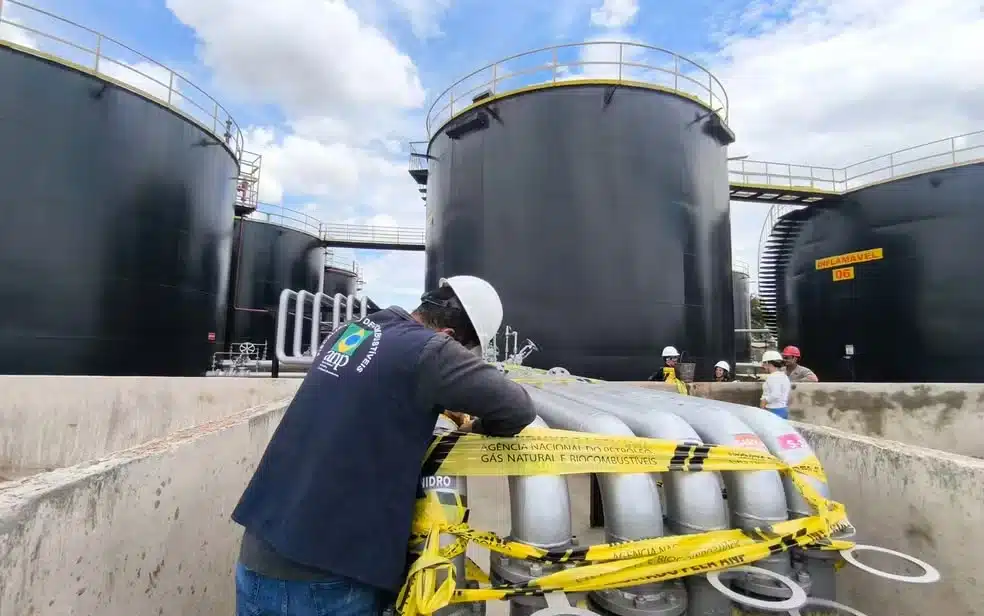 Técnico realizando inspeção em dutos de combustível em base de armazenamento com tanques industriais